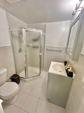 A bathroom with a glass shower enclosure, a toilet, and a sink with a gold faucet.