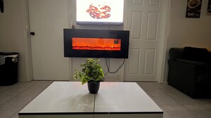 Una sala de estar con un televisor de pantalla plana montado en la pared, una planta en maceta sobre una mesa de centro blanca y un sofá negro.