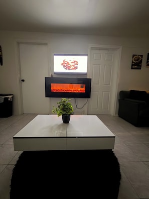 A living room with a flat-screen TV mounted on the wall, a potted plant on a white coffee table, and a black sofa.