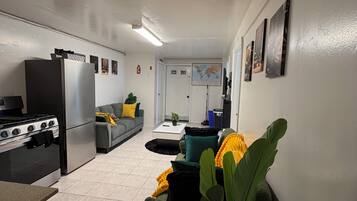 Ein kompakter Wohnbereich mit Küchenzeile, einer Couch, einem Couchtisch und einem Blumentopf.