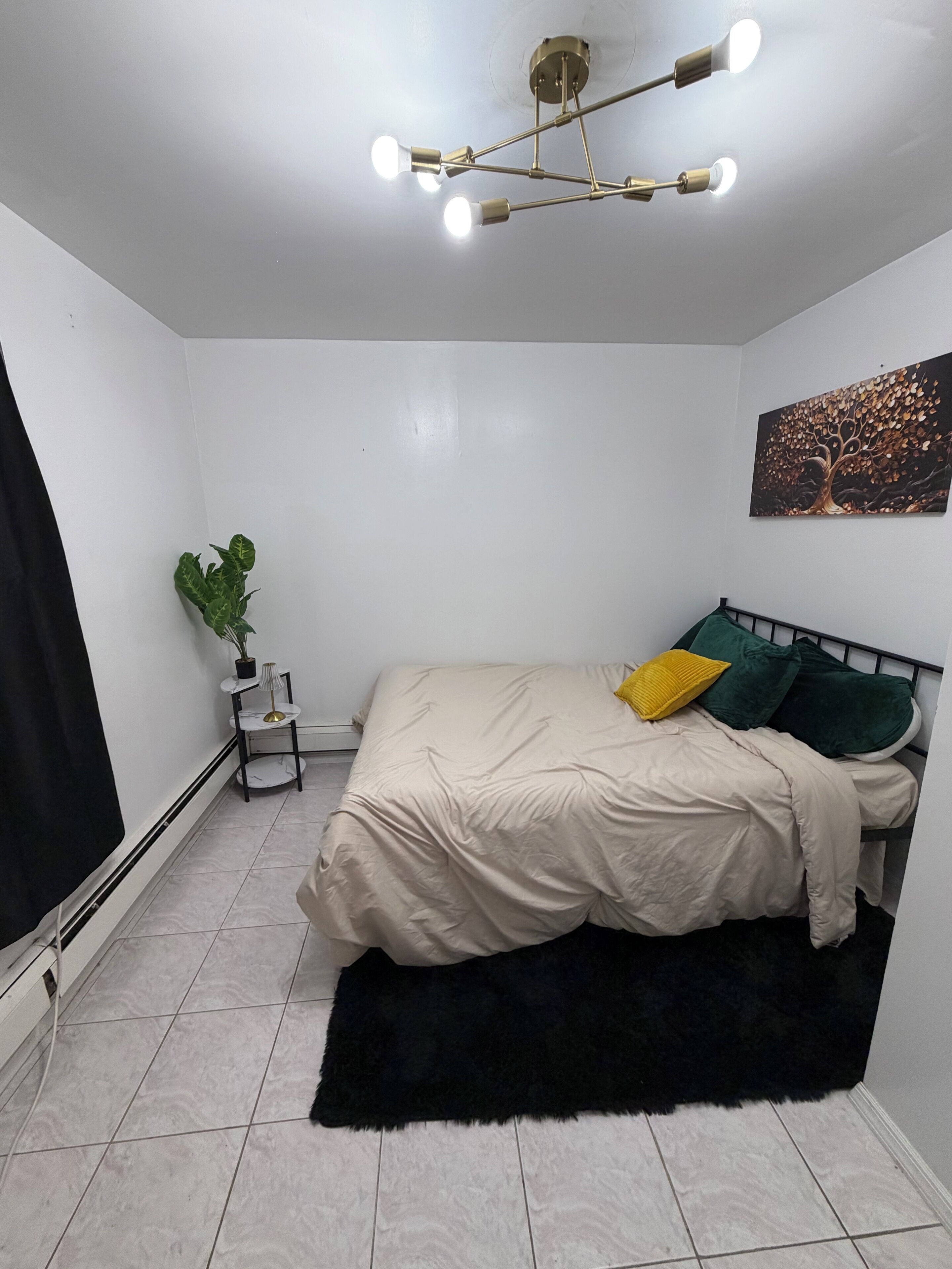 Ein Schlafzimmer mit einem Bett, einer Pflanze, einem Bild und einer Deckenleuchte.