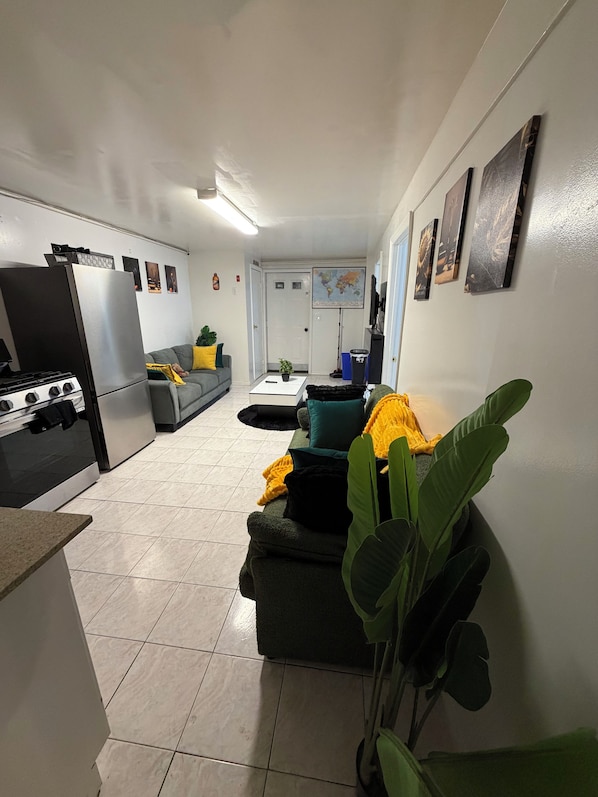 A modern kitchen with a refrigerator, stove, and microwave. There is a gray sofa with a yellow throw blanket and a green plant.