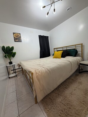 A bedroom with a bed, a nightstand, a potted plant, a ceiling light fixture, and a wall-mounted artwork.