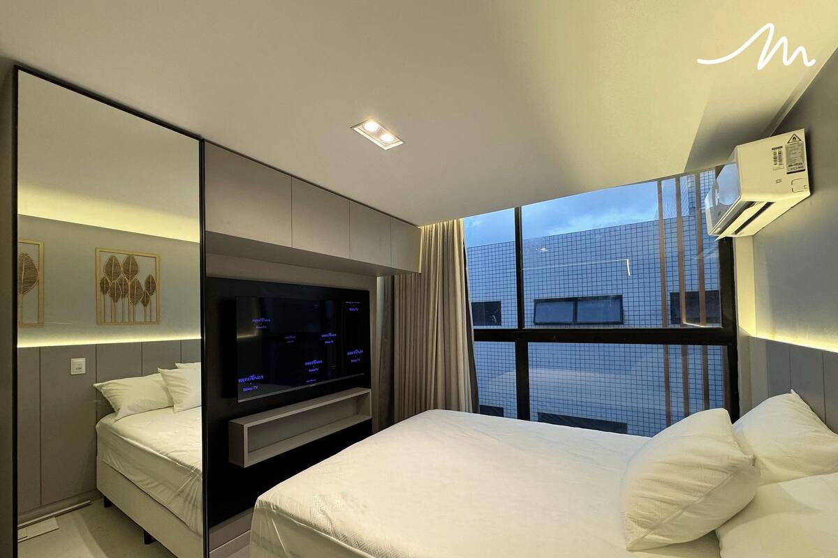 Una habitación de hotel moderna con una cama grande, un televisor de pantalla plana en la pared y una ventana con vista a la ciudad.