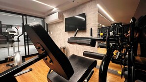 A gym with exercise equipment, a TV on the wall, and a wooden floor. - Breeze Miramar Hospedagens (Joao Pessoa)