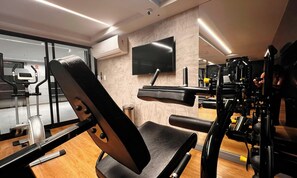 Een sportschool met trainingsapparatuur, een televisie aan de muur en een houten vloer.