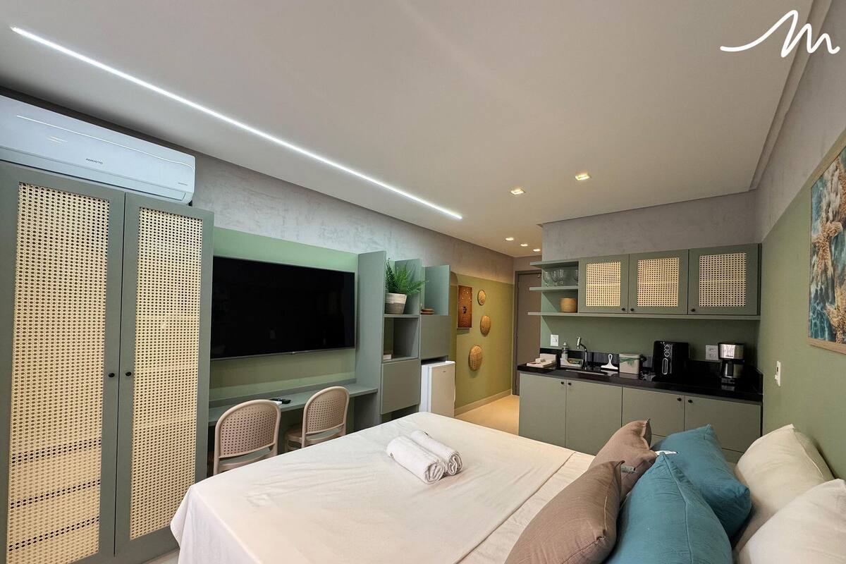 Una habitación de hotel moderna con una cama grande, un televisor de pantalla plana, una kitchenette y un área de comedor.