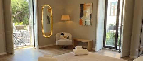 A modern bedroom with a large bed, a chandelier, a mirror, and a view of the outdoors.
