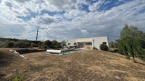 Een modern huis met een zwembad, omringd door droog gras en bomen.