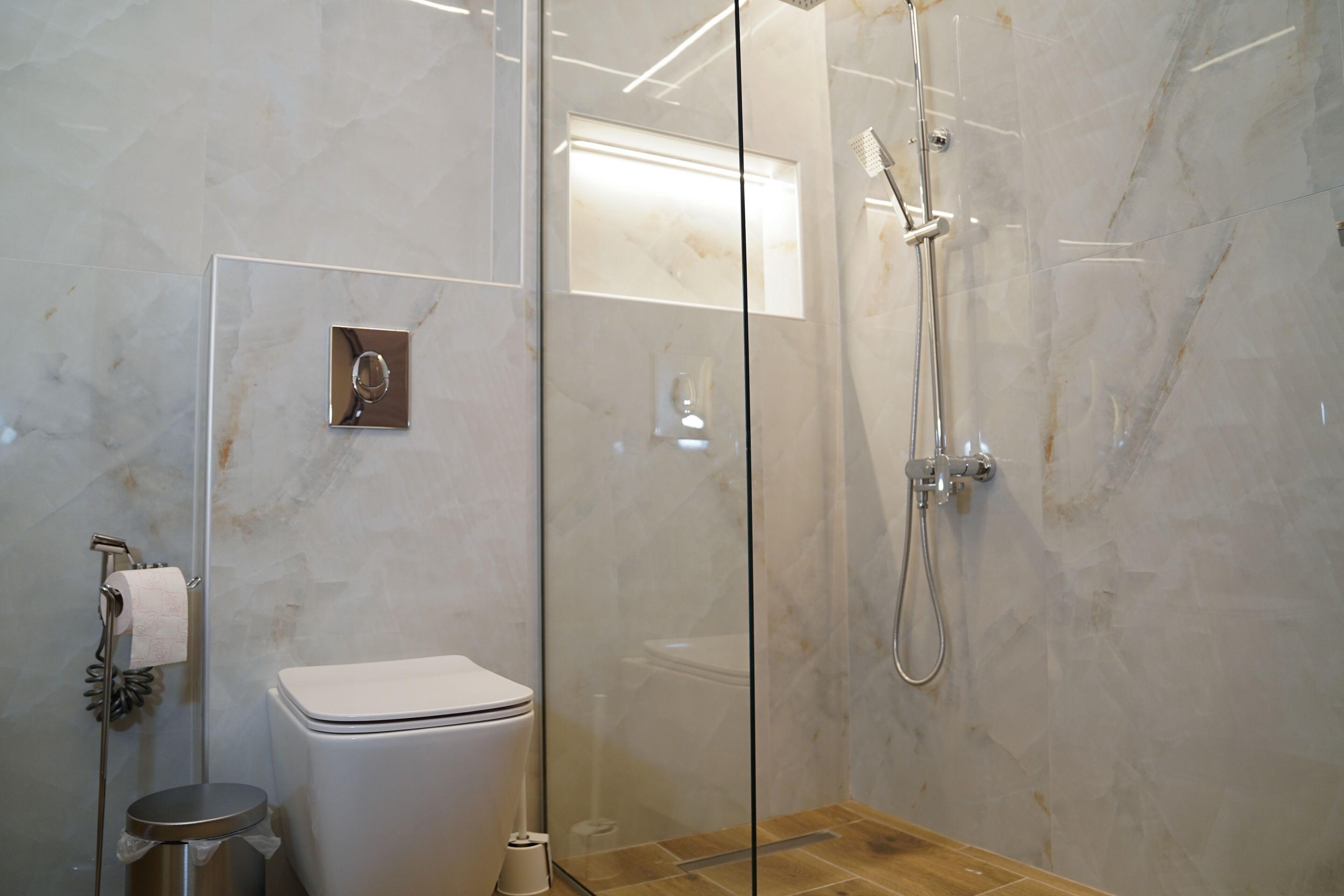 A modern bathroom with a glass-enclosed shower, a toilet, and a trash bin.