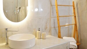 A modern bathroom with a large oval mirror, a round sink, and a wooden ladder shelf.
