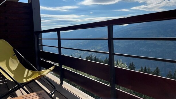 A balcony with a wooden floor, metal railing, and a yellow chair.