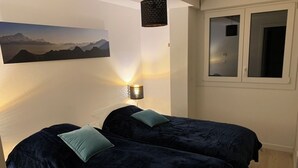 A bedroom with two beds, a wall-mounted lamp, and a window.