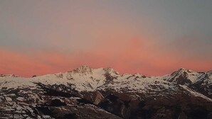A mountain range with snow-covered peaks under a pink sky.