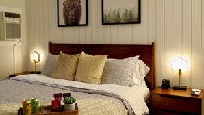 A neatly made bed with patterned pillows, a bedside table with a lamp, and framed pictures on the wall. - Local Gem w/ King, 65” TV, Hot Tub, Ski Bus (Park City)