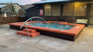 A rectangular outdoor hot tub with a metal ladder, a wooden deck, and a sign warning of no lifeguard on duty. - Local Gem w/ King, 65” TV, Hot Tub, Ski Bus (Park City)