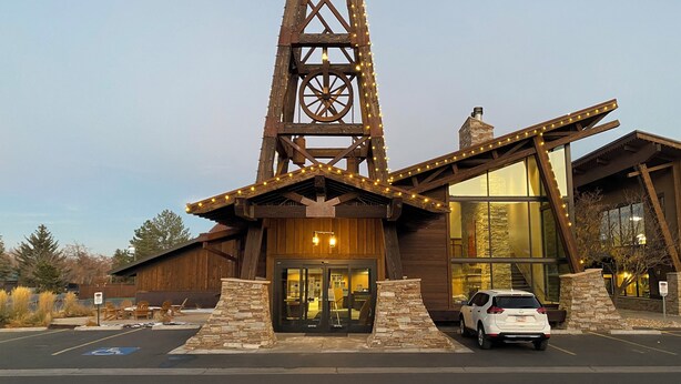 A rustic building with a prominent tower structure, large windows, and a parking area with a white car. - Local Gem w/ King, 65” TV, Hot Tub, Ski Bus (Park City)