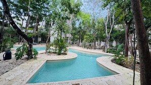 A swimming pool with a curved design, surrounded by trees and a stone pathway. - Beautiful apartment 10 minutes from the beach with Jacuzzi Swimming pools GYM Terraces. (TULUM)