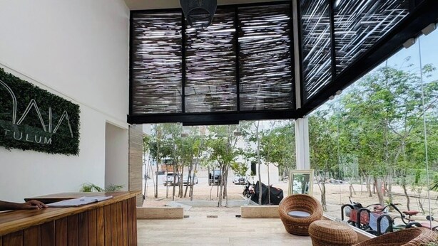 A reception area with a wooden reception desk, wicker chairs, and a glass partition. - Beautiful apartment 10 minutes from the beach with Jacuzzi Swimming pools GYM Terraces. (TULUM)