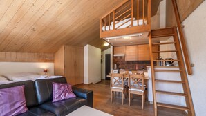 Une chambre de style loft avec un lit superposé, un escalier en bois, un coin repas avec une table et des chaises, et une kitchenette.