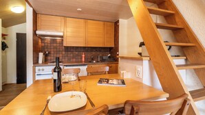 Une cuisine avec des meubles de rangement en bois, une table à manger avec des chaises, une bouteille de vin et un magazine.