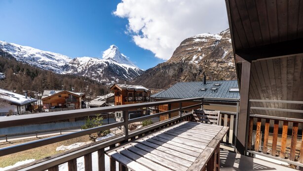 Une terrasse en bois offrant une vue sur des montagnes enneigées et un bâtiment de style chalet.