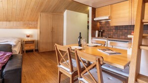 Une pièce chaleureuse et bien éclairée, avec une table à manger en bois, des chaises, une petite table de chevet avec une lampe et un lit.