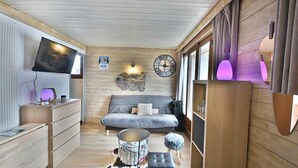 A cozy cabin interior with a wooden ceiling, a sofa, a television, and a wall clock. - 350m from ski slopes, 3rd floor, balcony, parking, ski locker, 24m², Les Gets (Les Gets)
