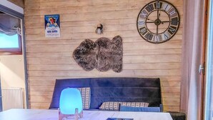 A cozy room with a wooden wall, a large clock, a poster, and a unique rug. - 350m from ski slopes, 3rd floor, balcony, parking, ski locker, 24m², Les Gets (Les Gets)