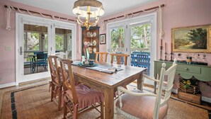 A dining area with a wooden table and chairs, a chandelier, and a view through large windows.