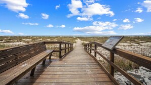 A wooden boardwalk leading to a beach with a signboard.