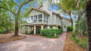 A two-story house with a brick driveway, surrounded by mature trees and a well-maintained garden.