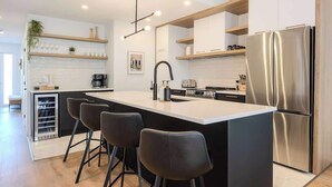 Una cocina moderna con una isla central, taburetes de bar, un refrigerador de acero inoxidable y electrodomésticos integrados.