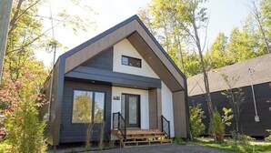 Una casa moderna de dos pisos con una entrada principal destacada, un pequeño porche y un número de casa visible.