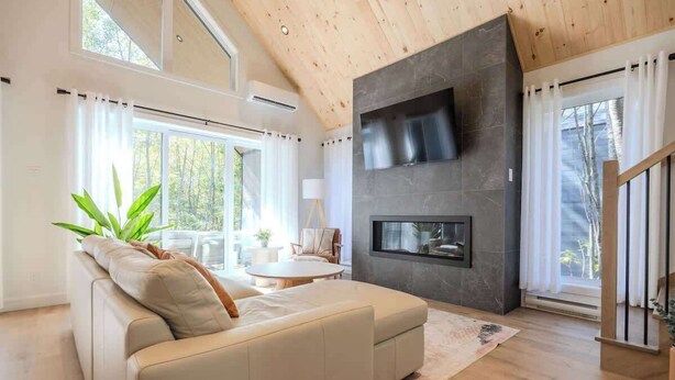 Una sala de estar moderna con sofá, chimenea y ventanas amplias.