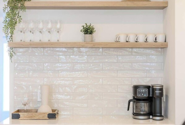 A kitchen with a white brick backsplash, wooden shelves, a coffee maker, and a potted plant.