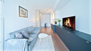 Una sala de estar moderna con un sofá gris, una mesa de centro blanca y un televisor que muestra una chimenea.