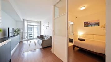 A modern apartment with a kitchen, living area, and bedroom. It features a sliding door, a sofa, a bed, and a painting on the wall.
