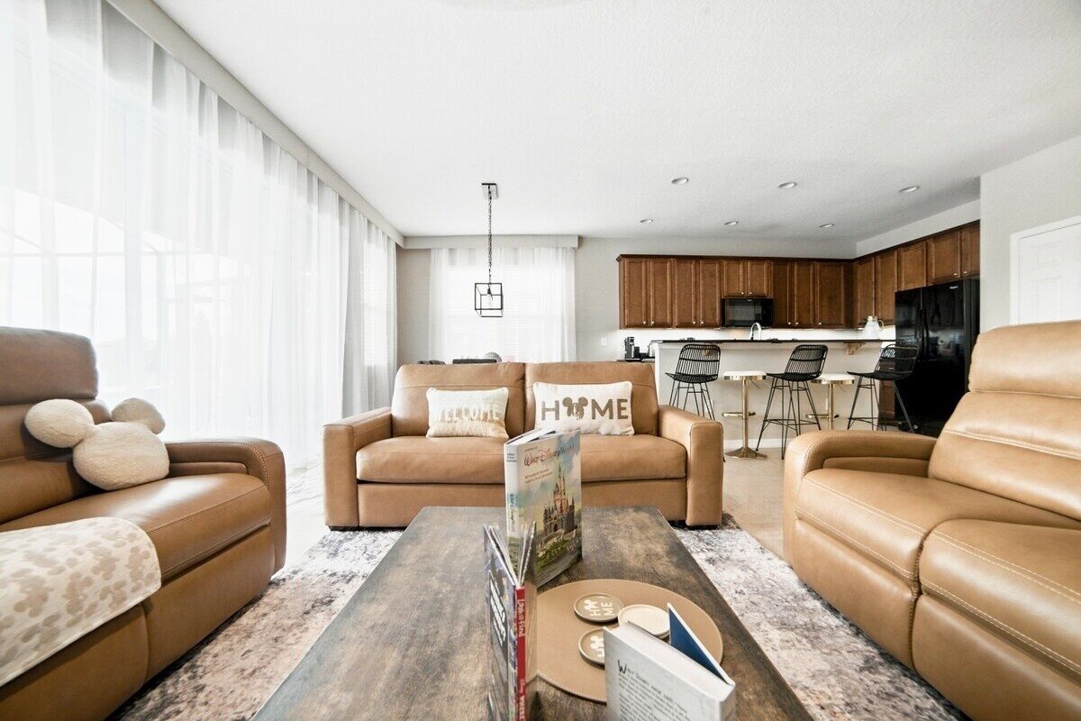 A modern living room with two leather sofas, a coffee table with books, and a kitchen in the background.