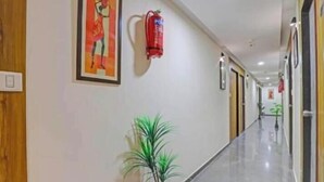 A hallway with a fire extinguisher, a framed artwork, and a potted plant. - hotel stay inn bopal (Ahmedabad)