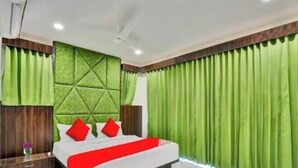 A bedroom with a bed, green curtains, and a decorative headboard. - hotel stay inn bopal (Ahmedabad)