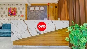 A reception area with a marble counter, a blue sofa, a wall clock, and a wooden panel. - hotel stay inn bopal (Ahmedabad)