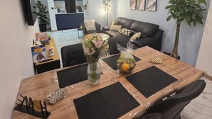 Un salon moderne avec un coin repas, comprenant une table à manger en bois, des chaises noires, un canapé en cuir noir et une grande plante en pot.