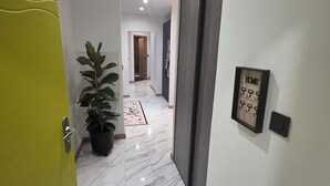 Un couloir avec un sol en marbre, une plante en pot, une porte et un panneau fixé au mur.