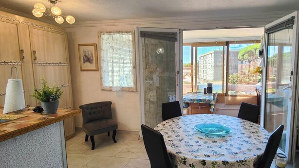 A compact kitchen with a round table, chairs, and a dining area with a view of buildings outside. - Nice 2P with Wifi & swimming pool near city center (Fréjus)