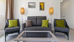 A modern living room with a grey sofa, two armchairs, and a coffee table. There are two floor lamps and two framed artworks on the wall. - Sunny Apartment Near Playamar Beach (Torremolinos)