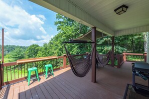 A covered outdoor deck with a hammock, two green stools, and a grill.