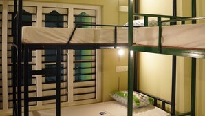 Une chambre avec un lit superposé doté d’une structure en métal vert, de draps blancs et d’une fenêtre ornée de vitraux décoratifs.