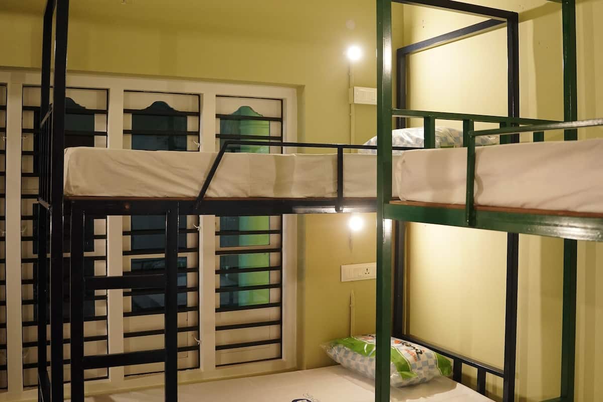 A bunk bed room with a green metal frame, white bedding, and a window with decorative glass panes.