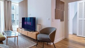 Una sala de estar moderna con un televisor de pantalla plana, un sillón cómodo, una mesa de centro de vidrio y piso de madera.